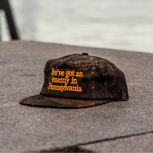 Camouflage cap with text on a stone surface with a blurred water background