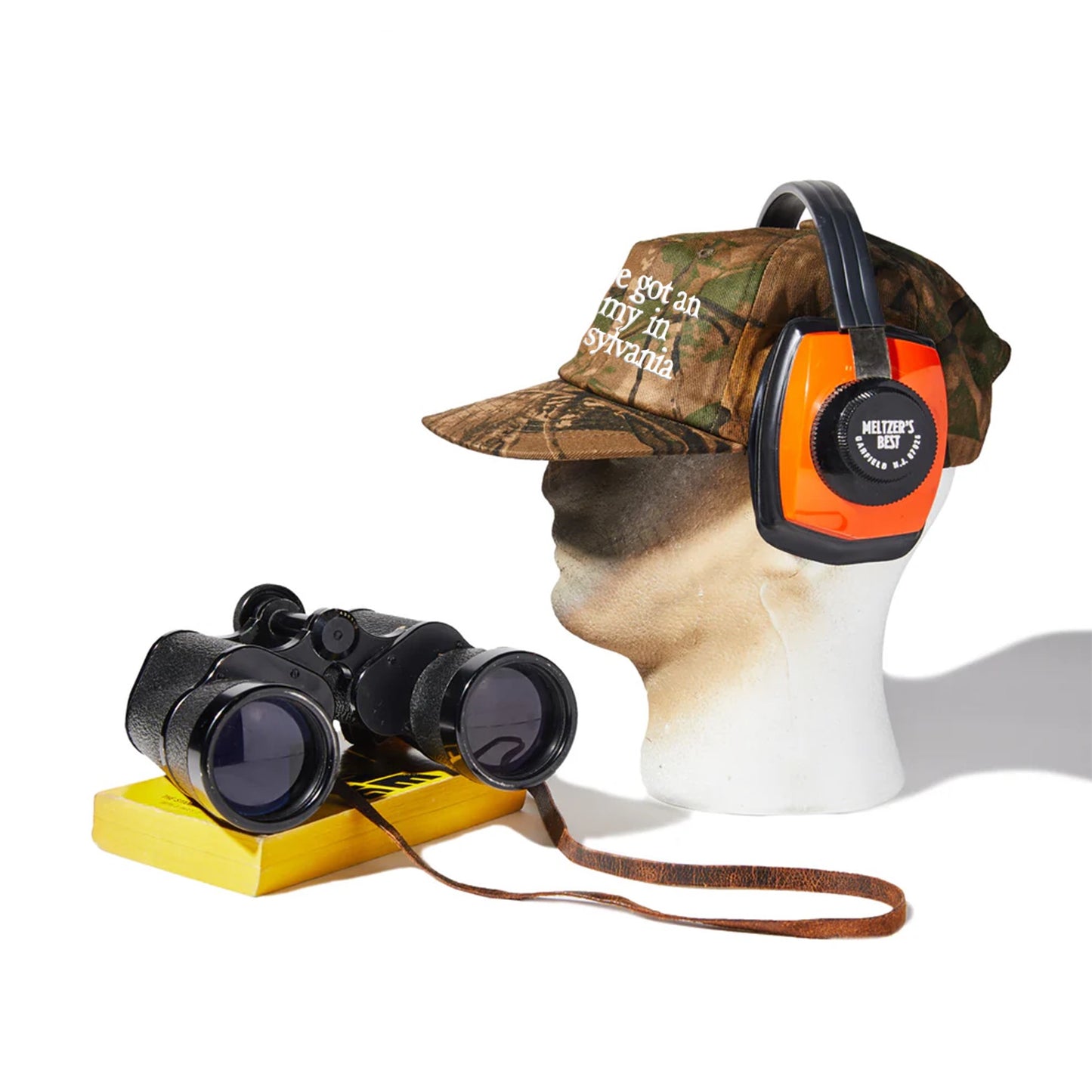 Mannequin head with camouflage cap, orange and black headphones, and binoculars on a white background