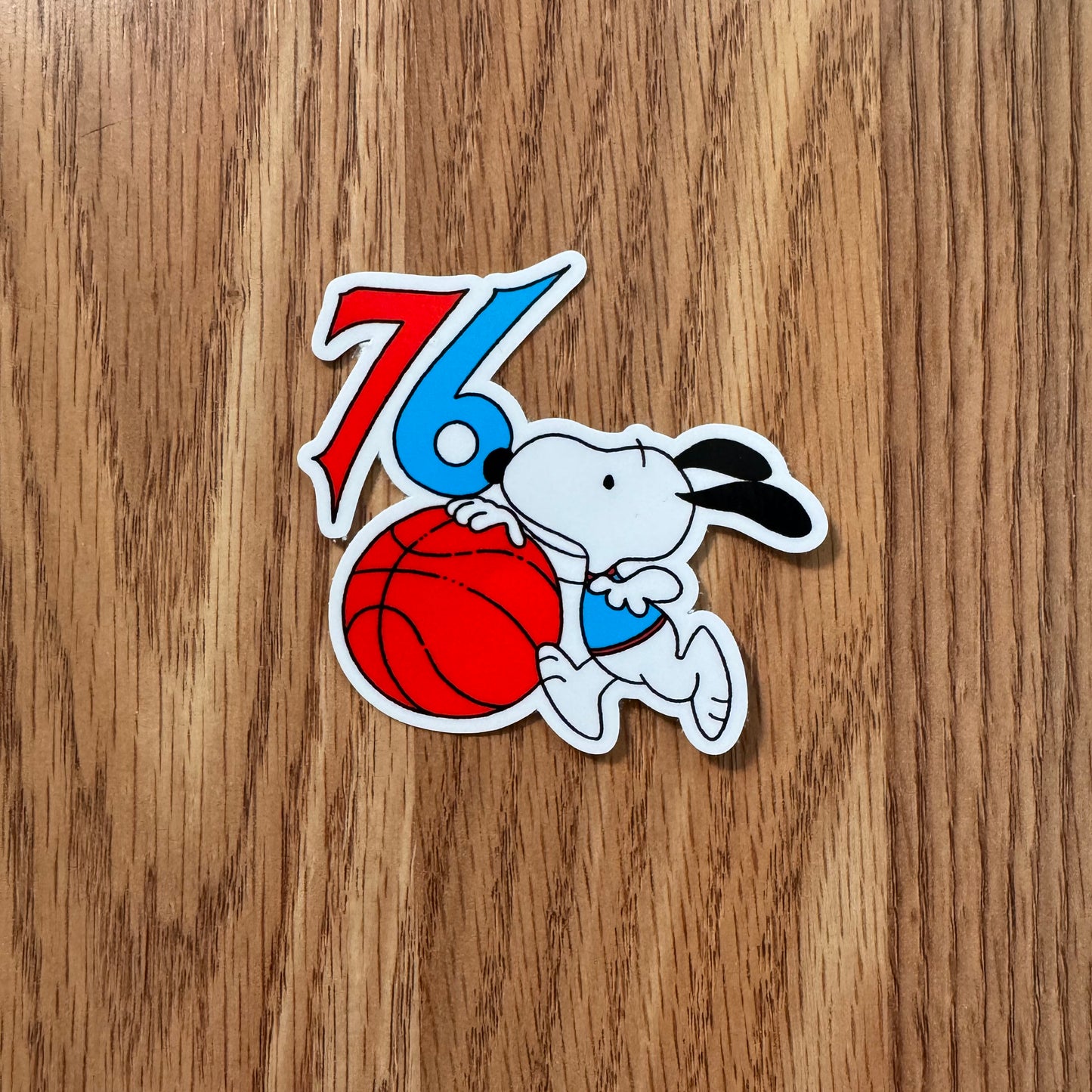 Sticker of a dog holding a basketball with '76' on a wooden surface