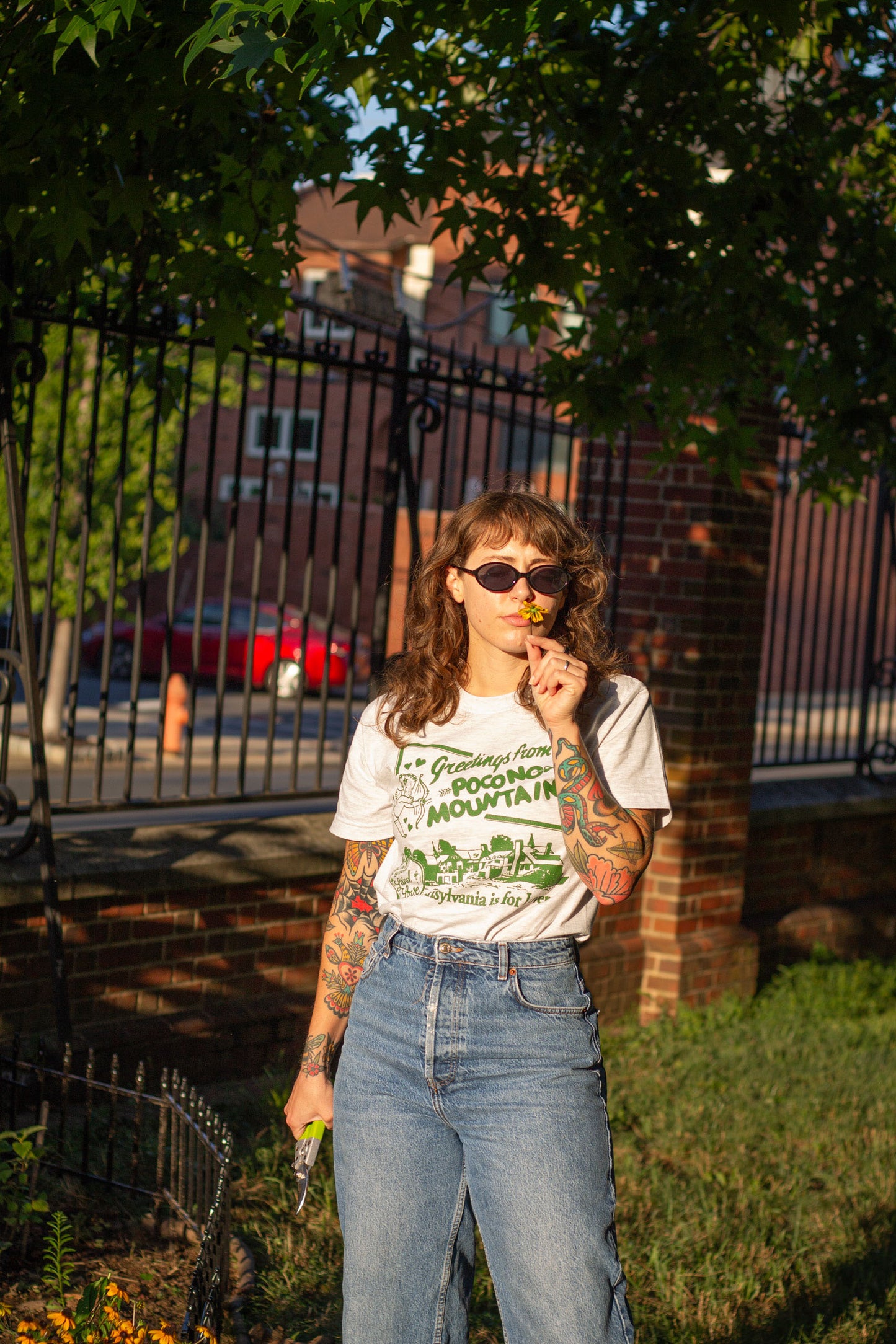 Person wearing a t-shirt with a graphic design, standing outdoors under trees.