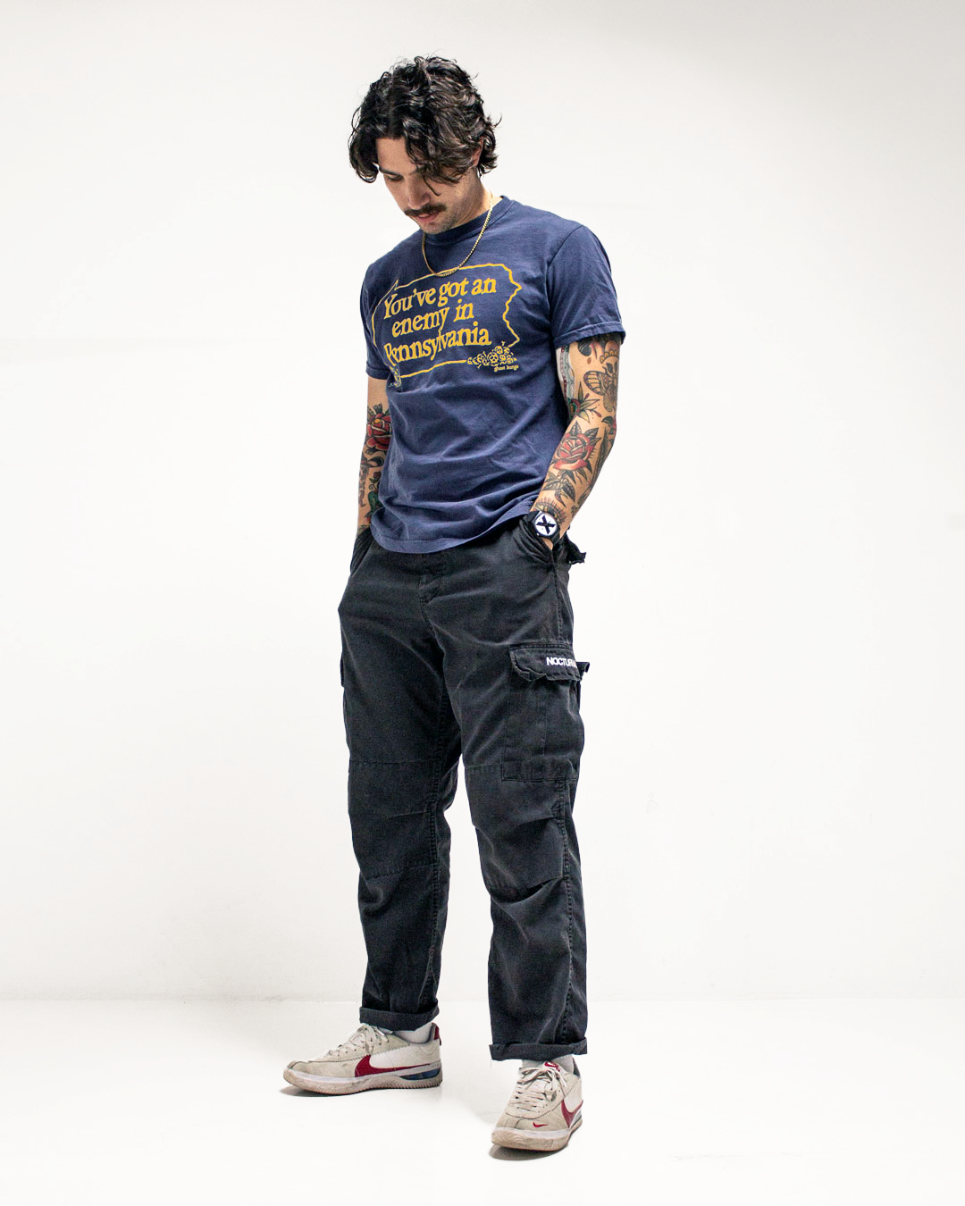 Person wearing a blue graphic t-shirt and dark cargo pants on a white background