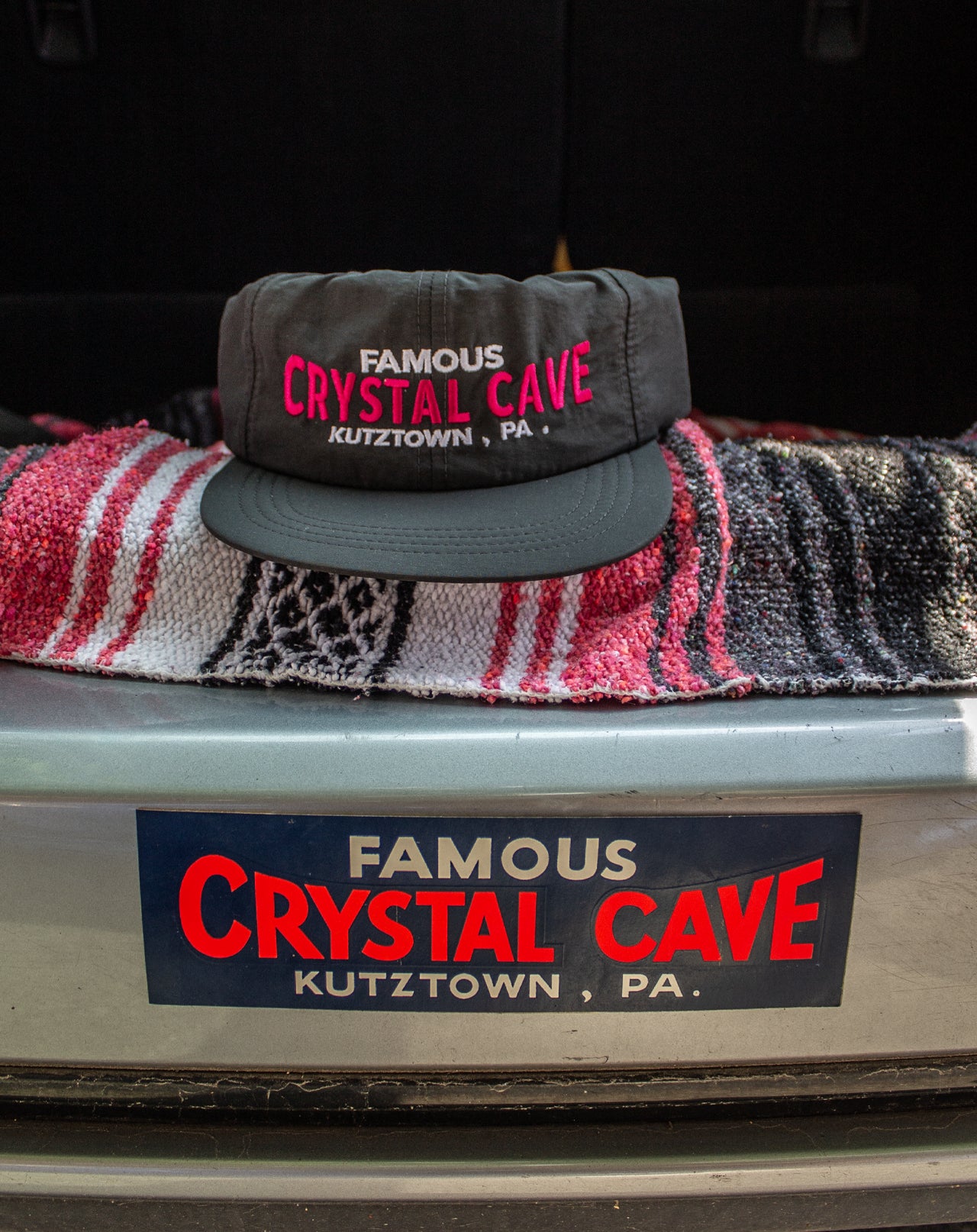 Black cap with 'Famous Crystal Cave' text on a vehicle's open trunk.