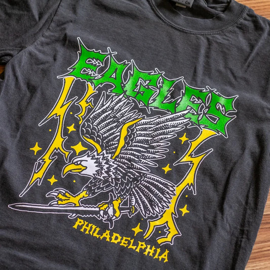 Black t-shirt with an eagle graphic and 'PHILADELPHIA' text on a wooden surface