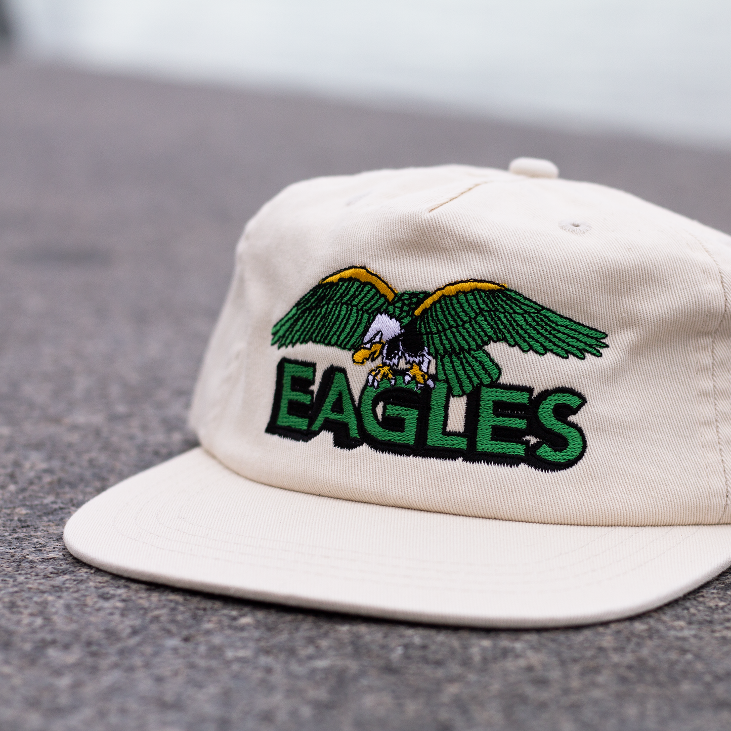 White cap with green and yellow eagle design and 'EAGLES' text on a gray surface