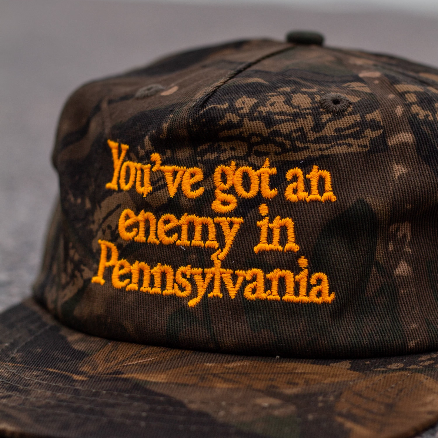 Camouflage cap with embroidered text 'You've got an enemy in Pennsylvania' on a gray background