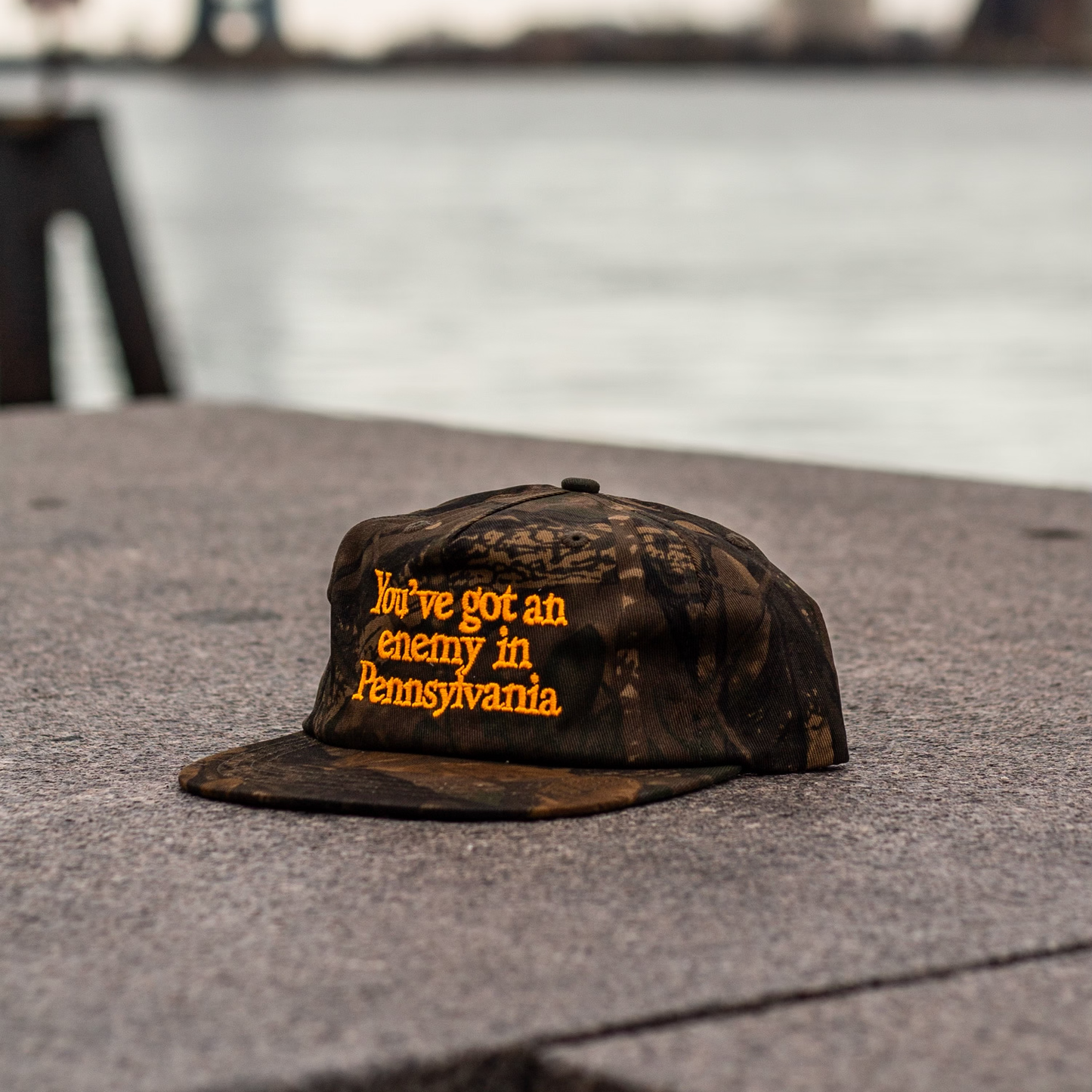 Camouflage cap with text on a stone surface with a blurred water background