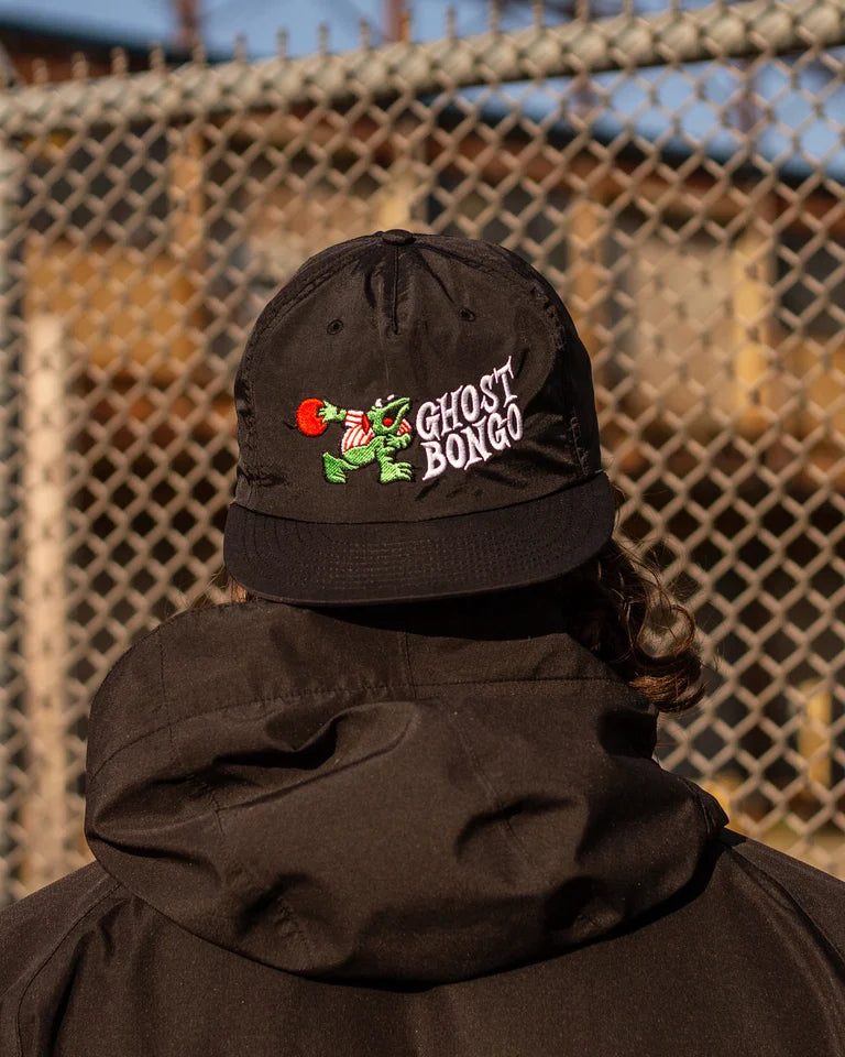 Person wearing a black cap with 'Ghost Box' logo against a chain-link fence background