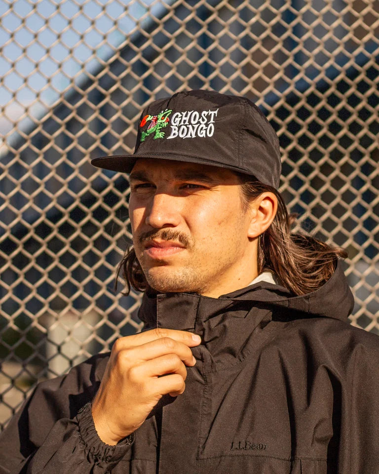 Man wearing a black cap with 'Ghost Bongo' logo against a chain-link fence.