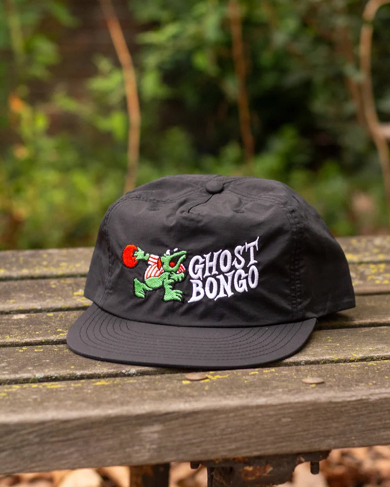 Black cap with 'Ghost Bongo' logo on a wooden surface with a blurred natural background