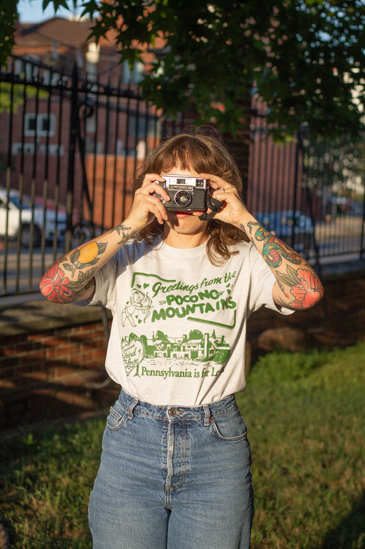 Person taking a photo with a vintage camera, wearing a t-shirt with Pocono Mountains text.