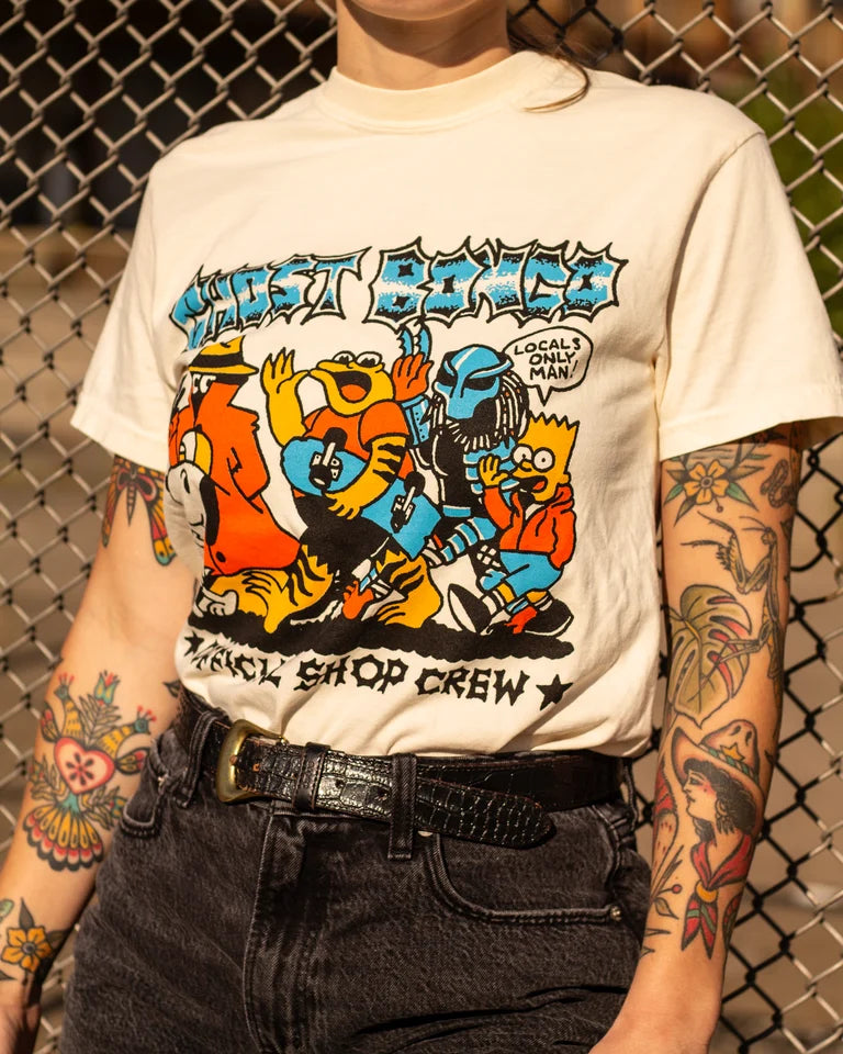 Person wearing a white t-shirt with colorful graphic design and text, standing against a chain-link fence.