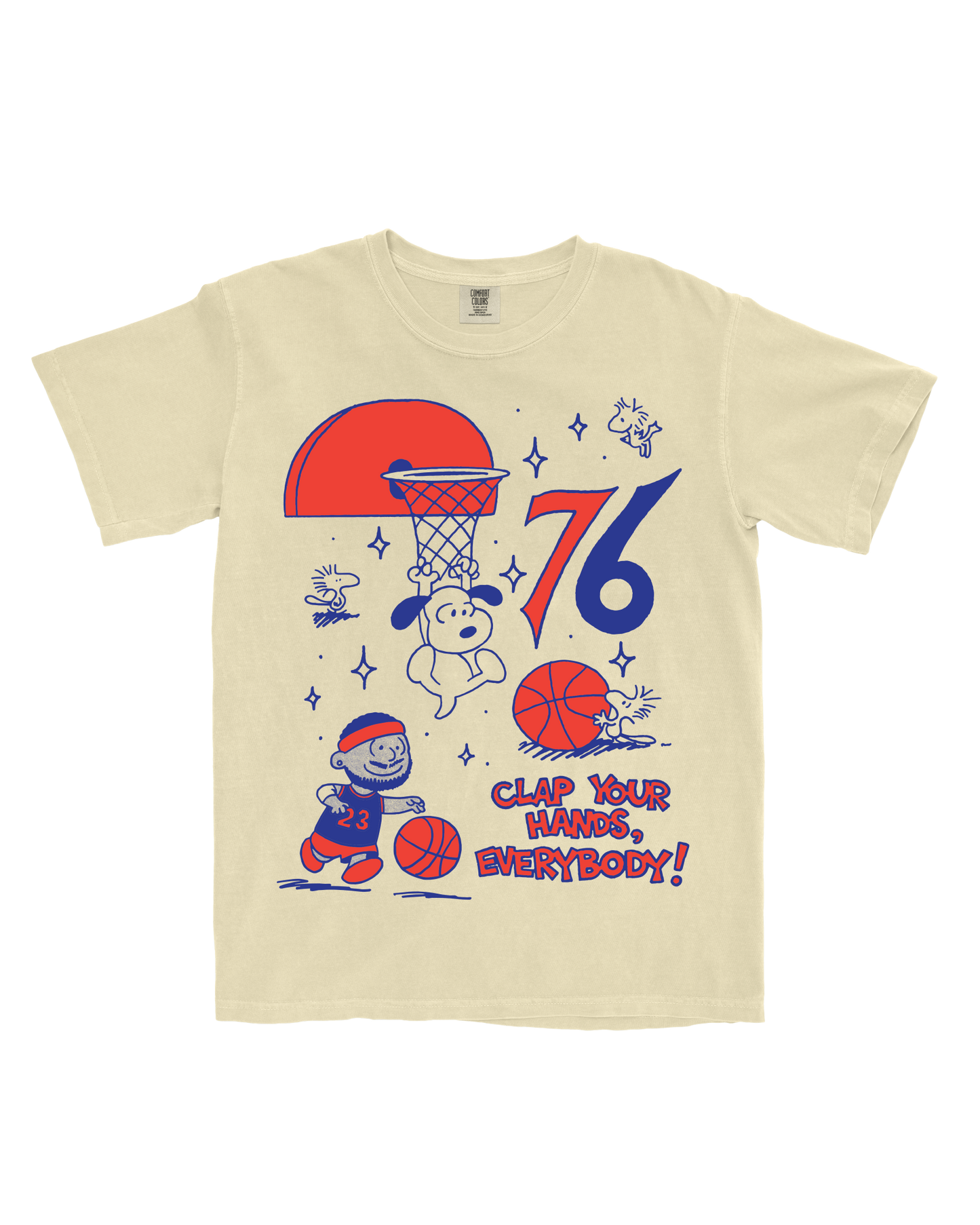 A cream-colored short-sleeve t-shirt featuring a colorful graphic print of Snoopy and Charlie Brown playing basketball, with the text 'CLAP YOUR HANDS, EVERYBODY!' and the numbers '76'.